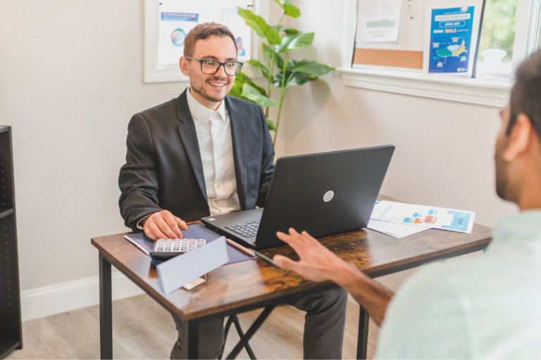 Business owner and broker discussing company valuation methods with financial reports and graphs on the desk.