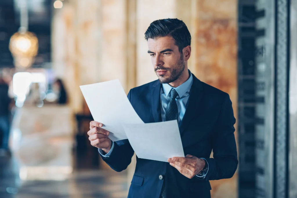 A well-dressed businessman intently reading a folded document, representing a client or broker reviewing the finalized engagement letter clauses.