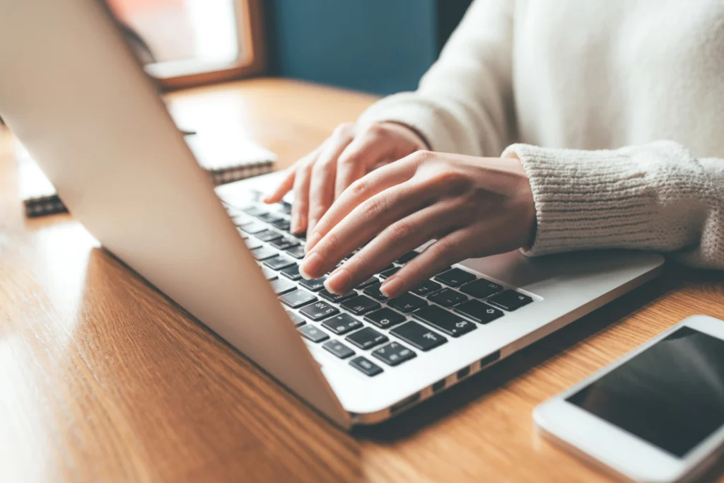 Close-up of hands typing on a laptop while drafting an engagement letter for selling a business.