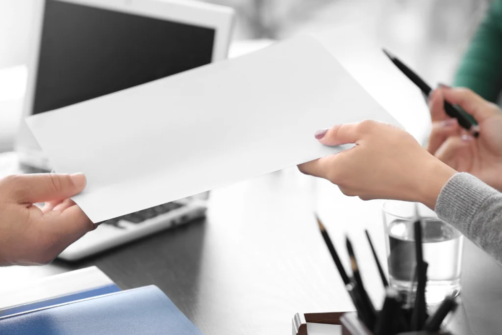 Two people exchanging and signing an engagement letter for selling a business during a meeting.