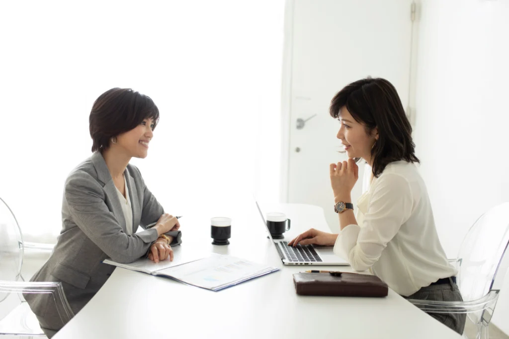 Two women in a business meeting smiling and discussing plans, reflecting trustworthy SMB broker traits.