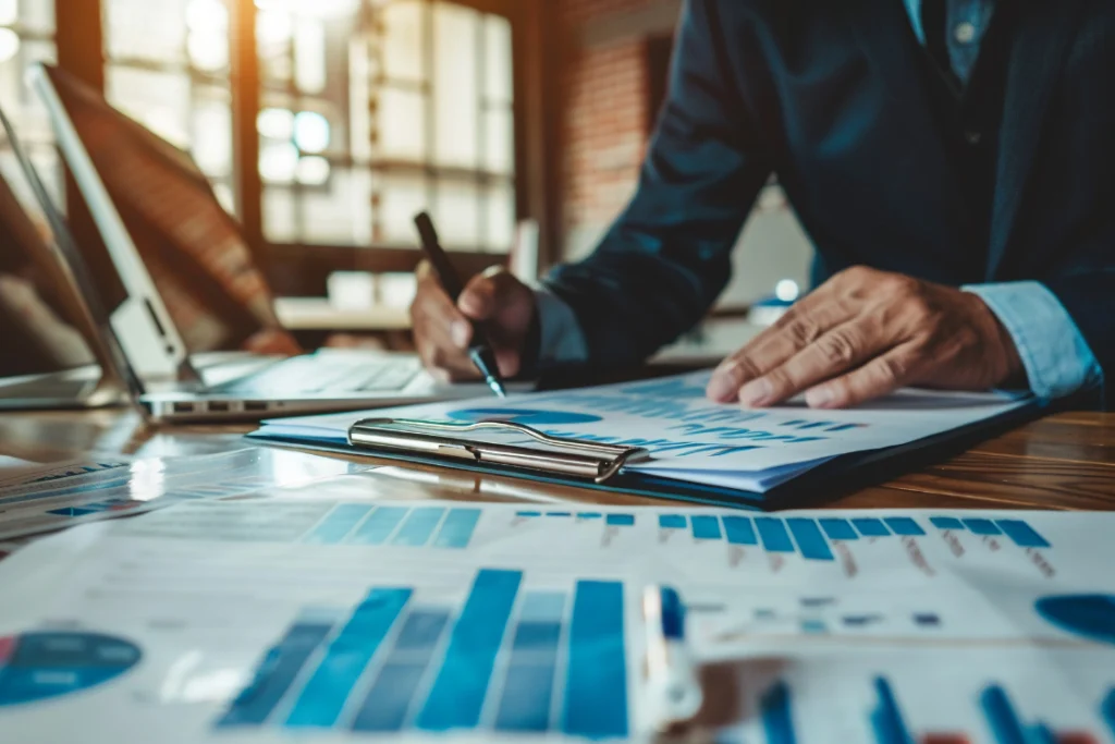 A business executive reviewing a paper with charts and graphs, using a pen to analyze data related to a business sale KPI tracker template.