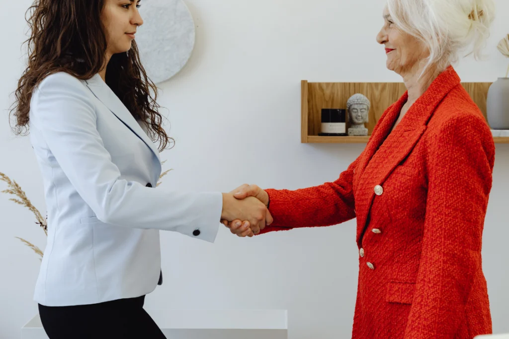 Two businesswomen in suits shaking hands to confirm a deal, representing a transition from lead to qualified buyer in a business sale.