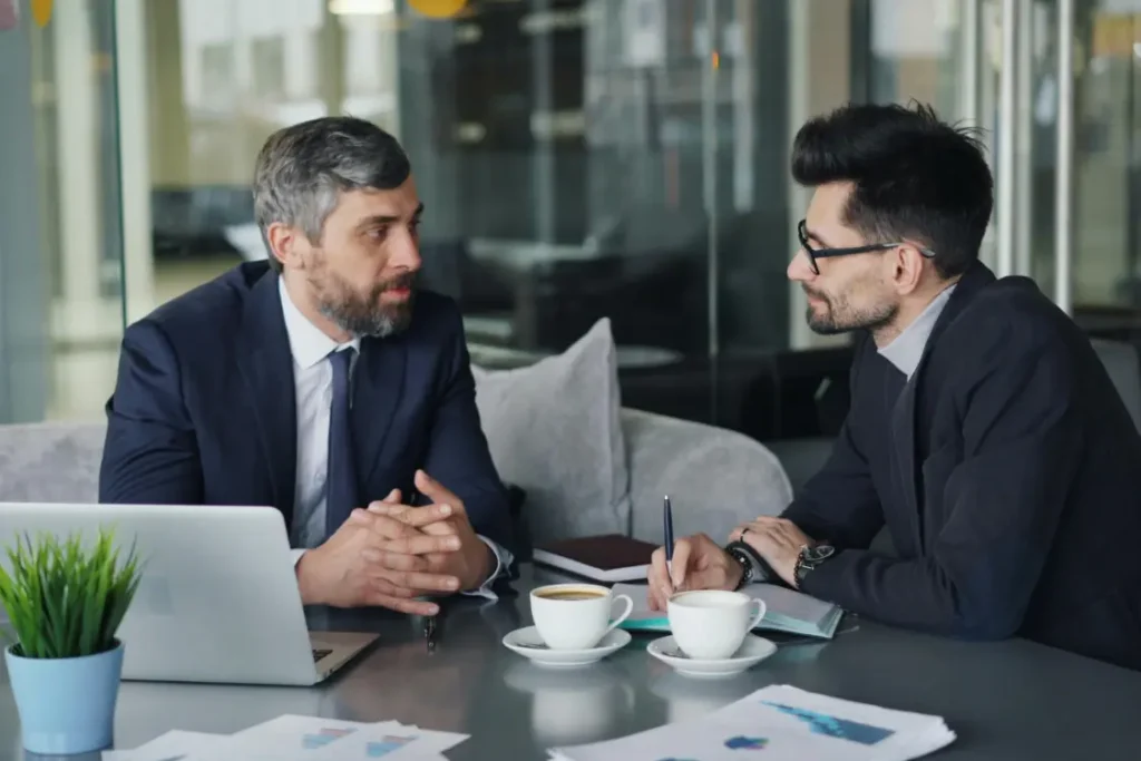 Two male business owners or consultants meet over coffee to discuss a financial strategy, representing the consultation stage of a private business valuation by an expert.