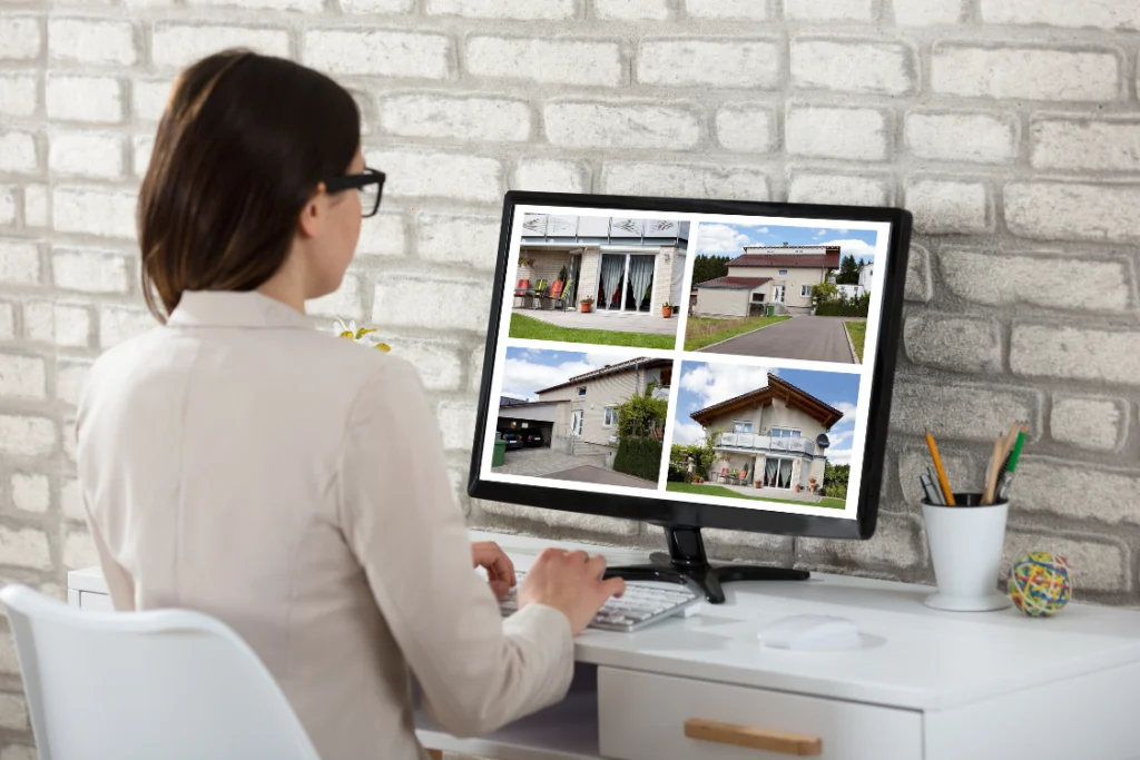 A woman in business attire looking at a computer monitor displaying four different house listings, symbolizing a qualified buyer actively researching business or property listings after the business listing launch date.