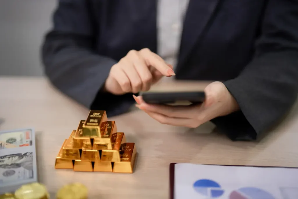 Close-up of a business professional checking a mobile device next to a stack of gold bars and money, illustrating the estimation of private business valuation and market worth.