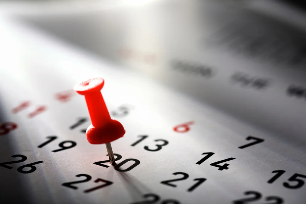 A red push pin marking the 20th on a calendar, emphasizing the importance of a specific, non-negotiable business listing launch date or deadline.