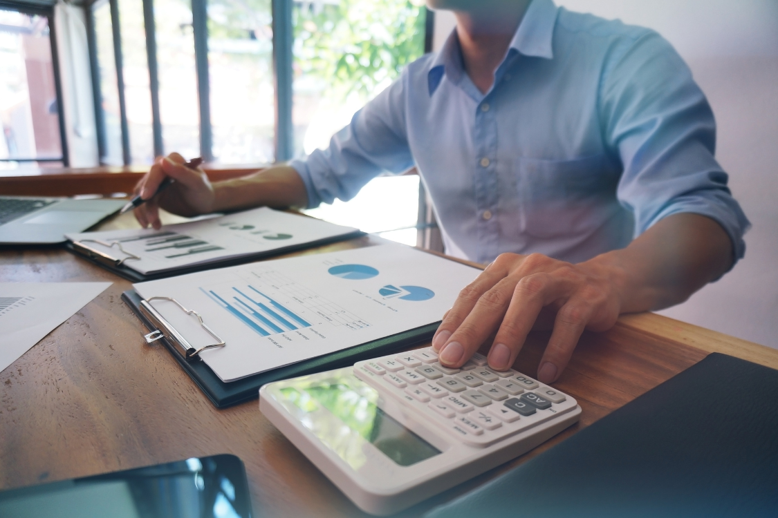 A professional using a calculator and reviewing a financial report with charts, demonstrating the work of a valuation expert in determining business valuation fees.