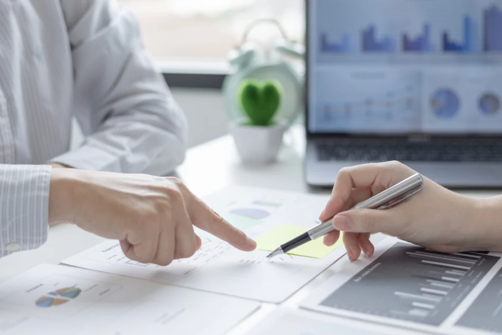 Two sets of hands reviewing financial charts and records, a step required for the financial analysis that influences business valuation fees.