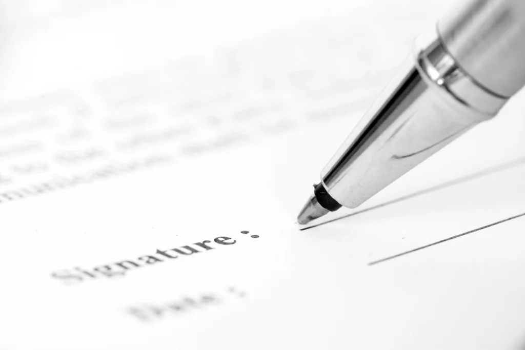 A close-up, black and white shot of a pen poised above the "Signature" line on a sample engagement letter for business sale document, highlighting the legal execution.