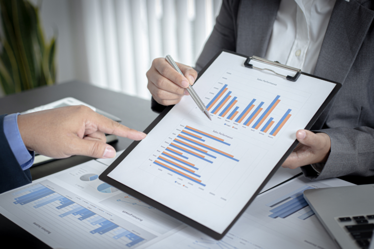 Two business people are looking at graphs on a clipboard.