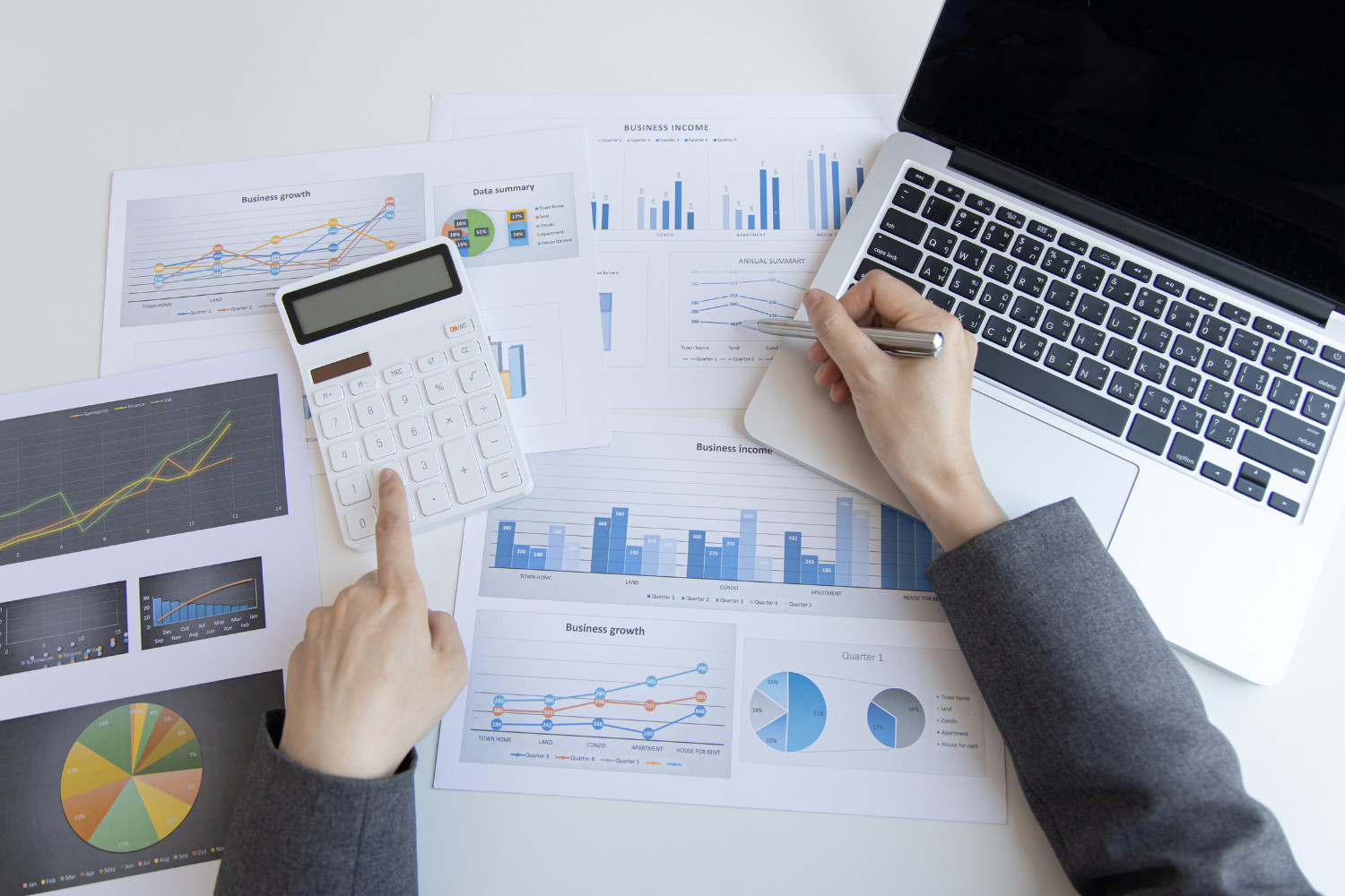 Overhead shot of an open laptop, graphs, and a hand using a calculator.