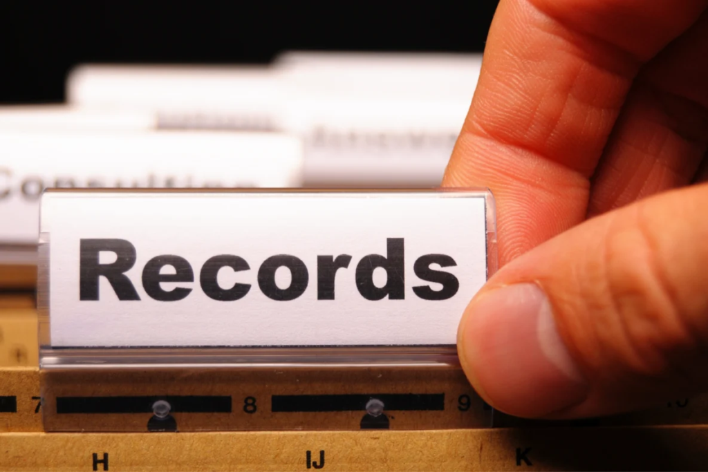 A hand is selecting a file folder labeled "Records" from a filing cabinet.