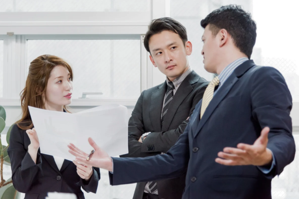 Three business professionals in suits are gathered around a document, engaged in a discussion.