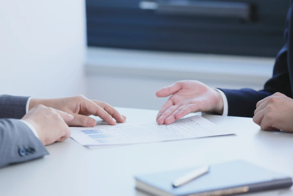 Two people in suits discussing documents on a white table, reflecting what due diligence do buyers do on my business.