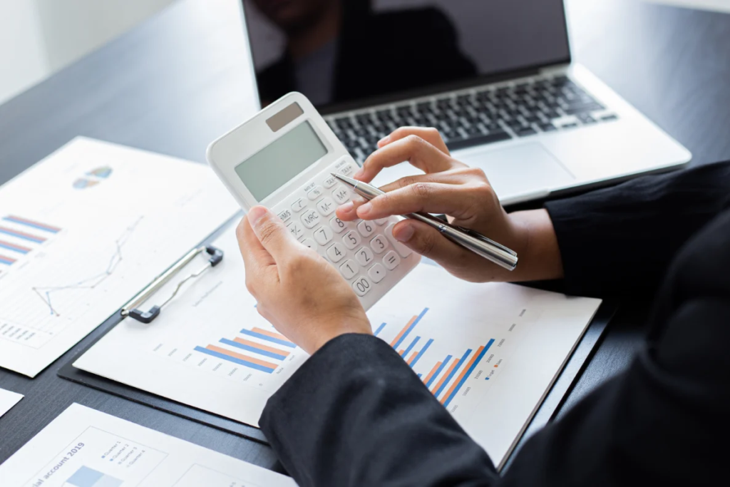 A person in a black suit uses a calculator to review financial charts and graphs on the table, reflecting what is a valuation.