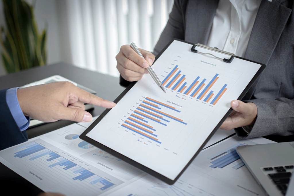 Two people are reviewing a chart with bar graphs on a clipboard in an office setting.