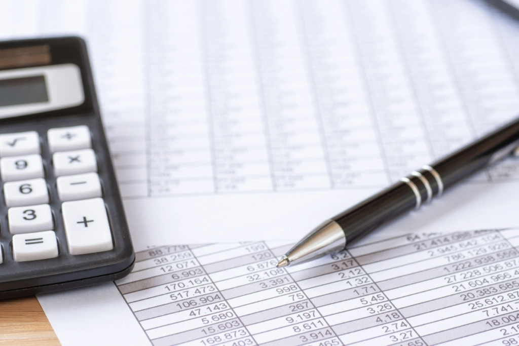 A black ballpoint pen rests on a spreadsheet next to a calculator.