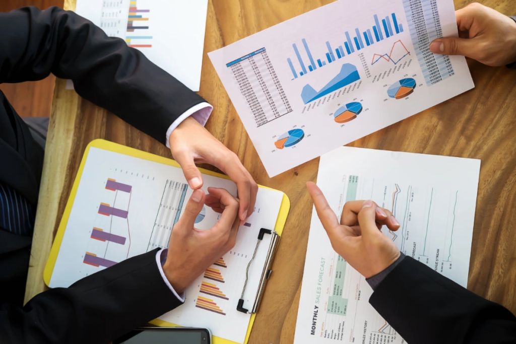 A group of people in business attire reviewing financial reports with charts and graphs on a wooden table.