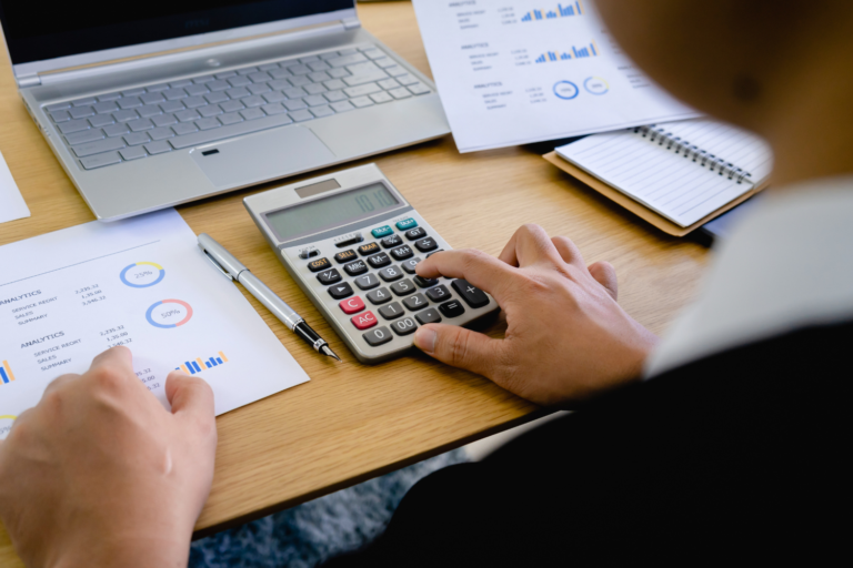 Person analyzing charts and financial data with calculator and laptop, illustrating how to calculate wealth gap in business planning.