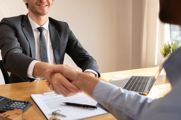 How to know when to sell your business illustrated by two professionals shaking hands over a contract and keys in an office setting