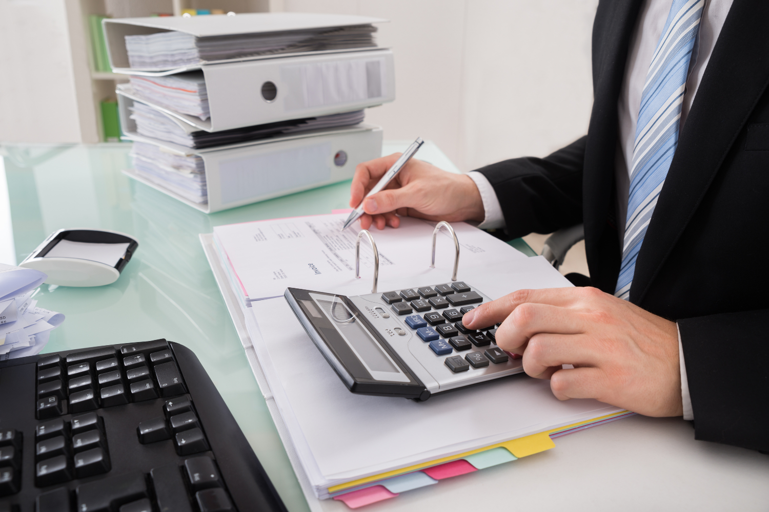 A CPA in a suit uses a calculator to review financial records and binders, the type of bookkeeping cleanup that affects quality of earnings report cost.