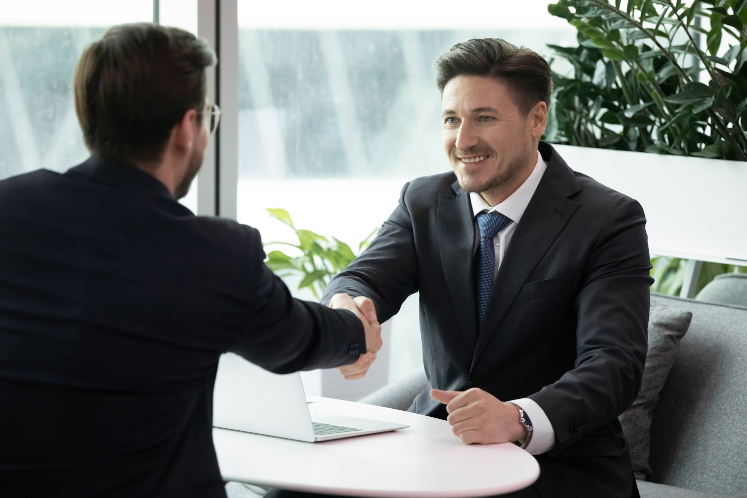 Two business professionals shaking hands in an office meeting, representing formal customer agreements and due diligence in a business sale.