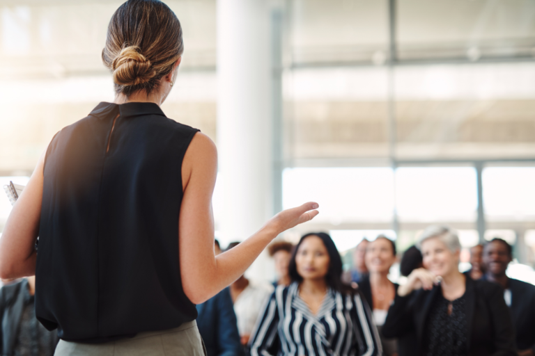 A business owner addresses a room of clients and team members, illustrating how diversifying relationships beyond the owner reduces business valuation customer concentration risk before a sale.