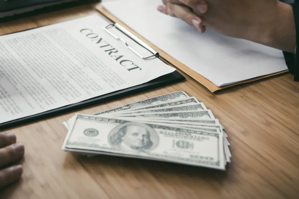 A contract document and stack of cash on a desk, representing the financial verification and contract review buyers conduct during due diligence when selling a business.