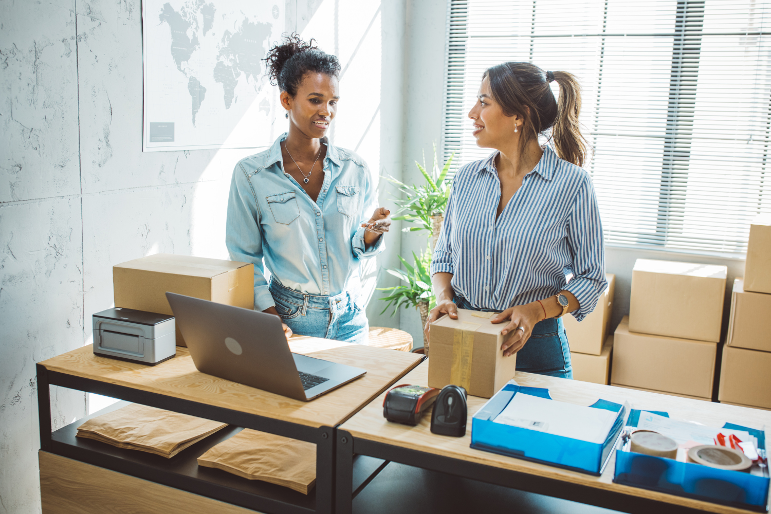 Two team members working with packages, a laptop, and shipping supplies, representing reduced key person risk through documented team operations.