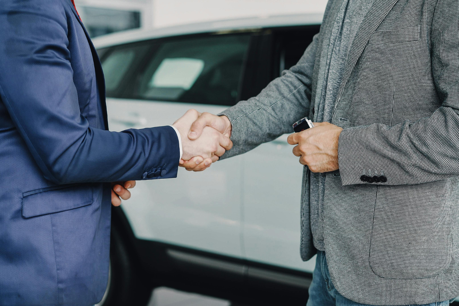 Two businesspeople shaking hands beside a car during a sale or deal negotiation.